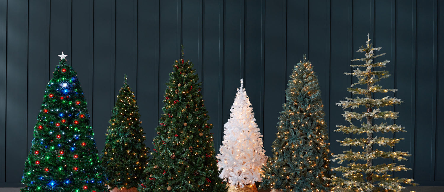 Five Christmas trees of different designs and colors against a dark wooden panel background.